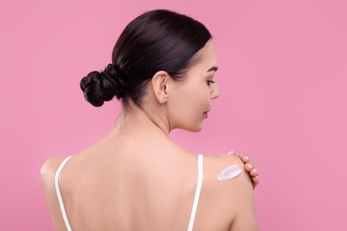 Photo of Beautiful woman with smear of body cream on her shoulder against pink background, back view