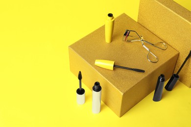 Different mascaras and eyelash curler on yellow background. Makeup product