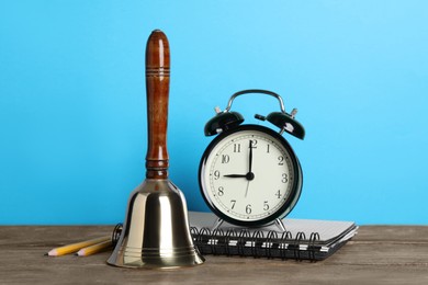 Photo of Golden bell, alarm clock and school stationery on wooden table against turquoise background