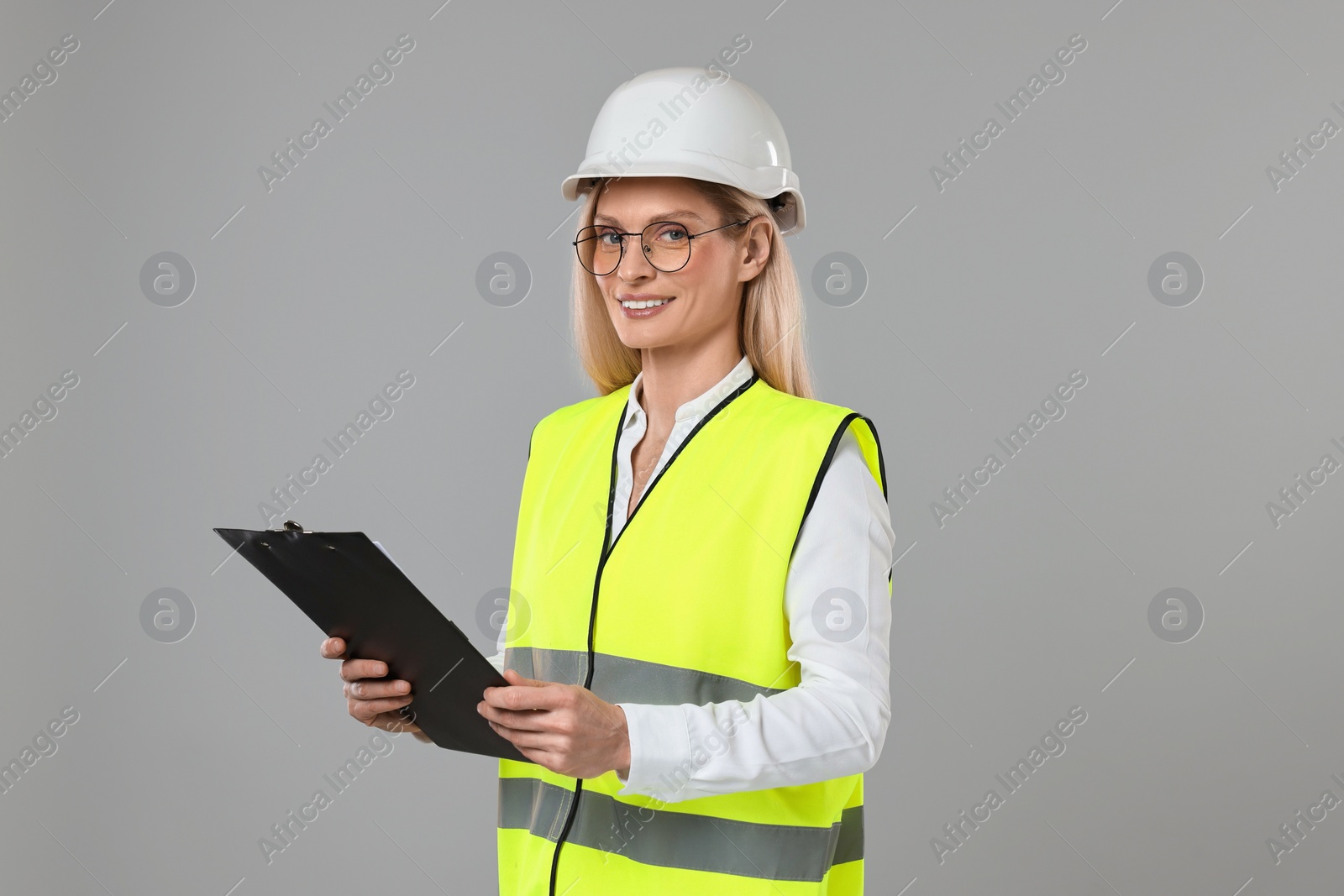 Photo of Engineer in hard hat holding clipboard on grey background