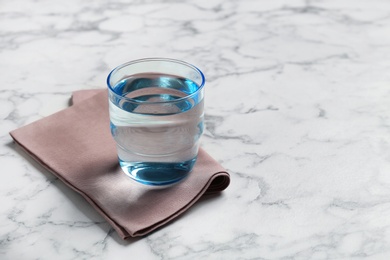 Photo of Glass with fresh water and napkin on marble table. Space for text