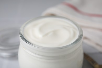 Photo of Delicious natural yogurt in glass jar on table, closeup