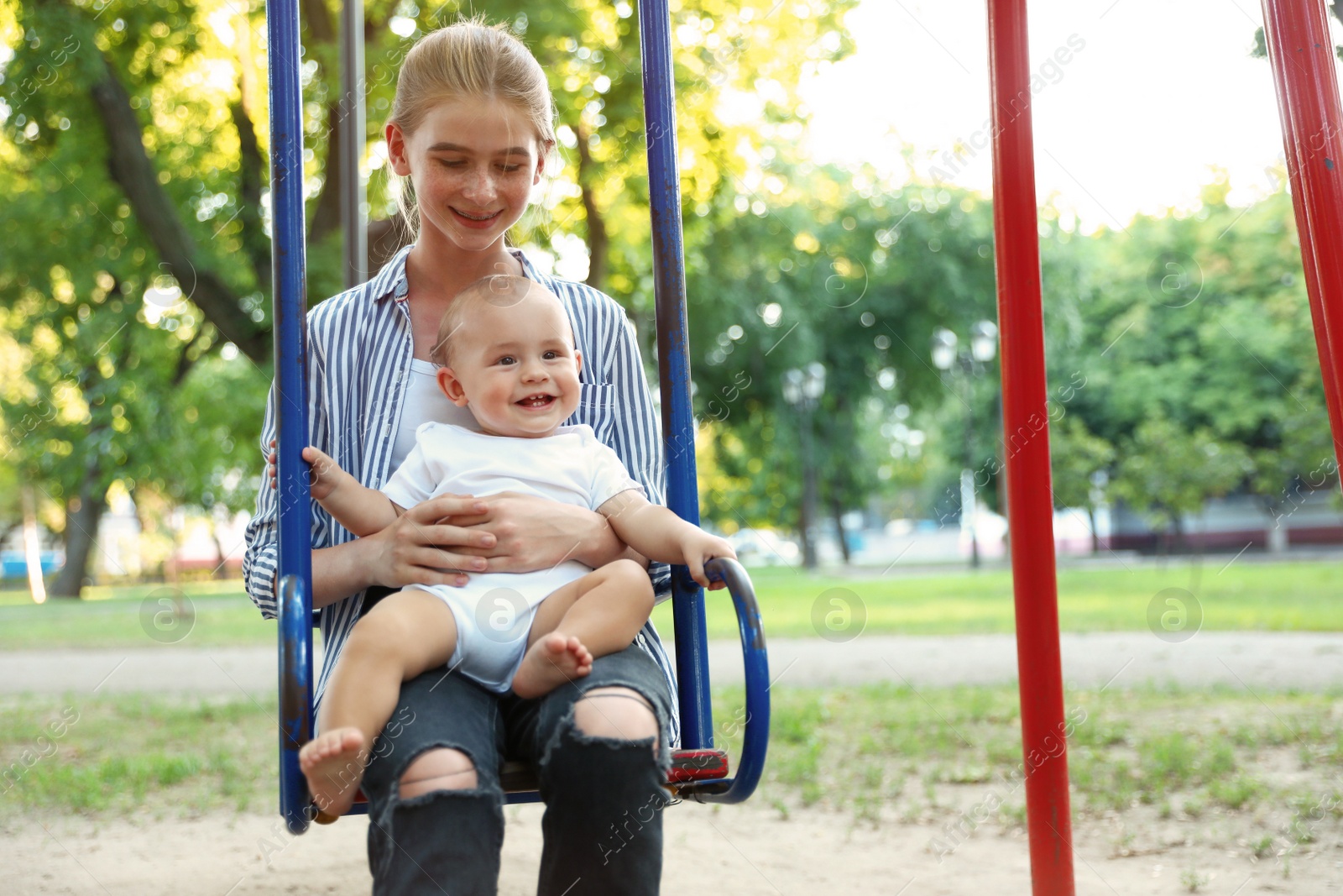 Photo of Teen nanny with cute little baby on swing outdoors