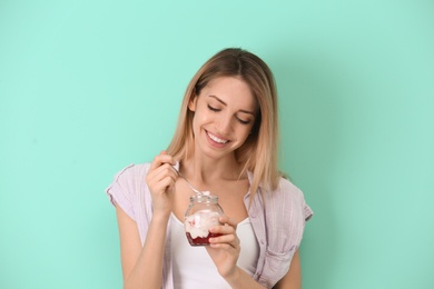 Photo of Young attractive woman eating tasty yogurt on color background