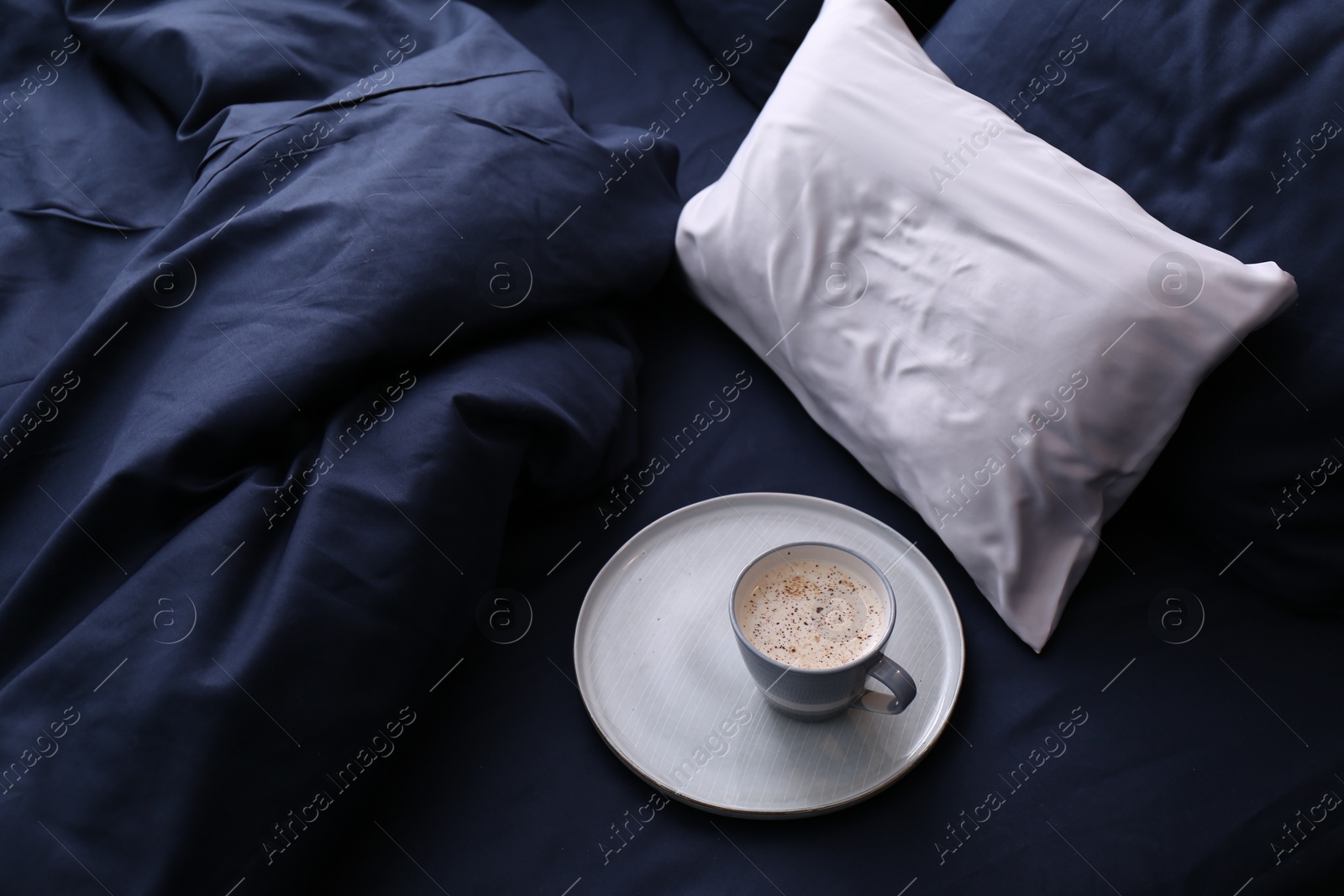 Photo of Cup of coffee on bed with stylish silky linens