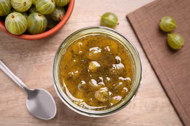 Photo of Jar of delicious gooseberry jam and fresh berries on wooden table, flat lay