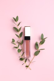 Bright lip gloss and green twigs on pink background, top view