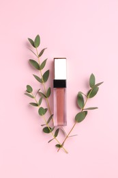 Photo of Bright lip gloss and green twigs on pink background, top view