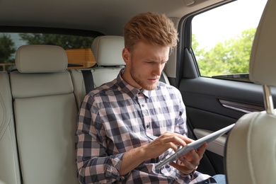 Photo of Attractive young man using tablet in luxury car