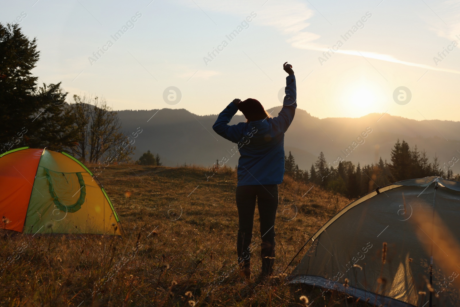 Photo of Woman stretching near camping tents in mountains at sunrise