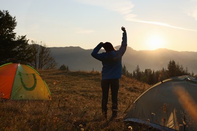 Photo of Woman stretching near camping tents in mountains at sunrise