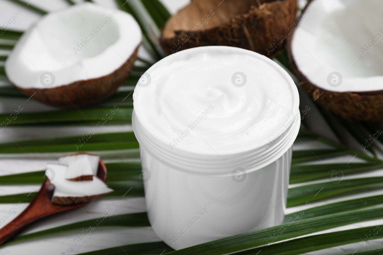 Photo of Jar of body cream with palm leaf and coconut on table, closeup