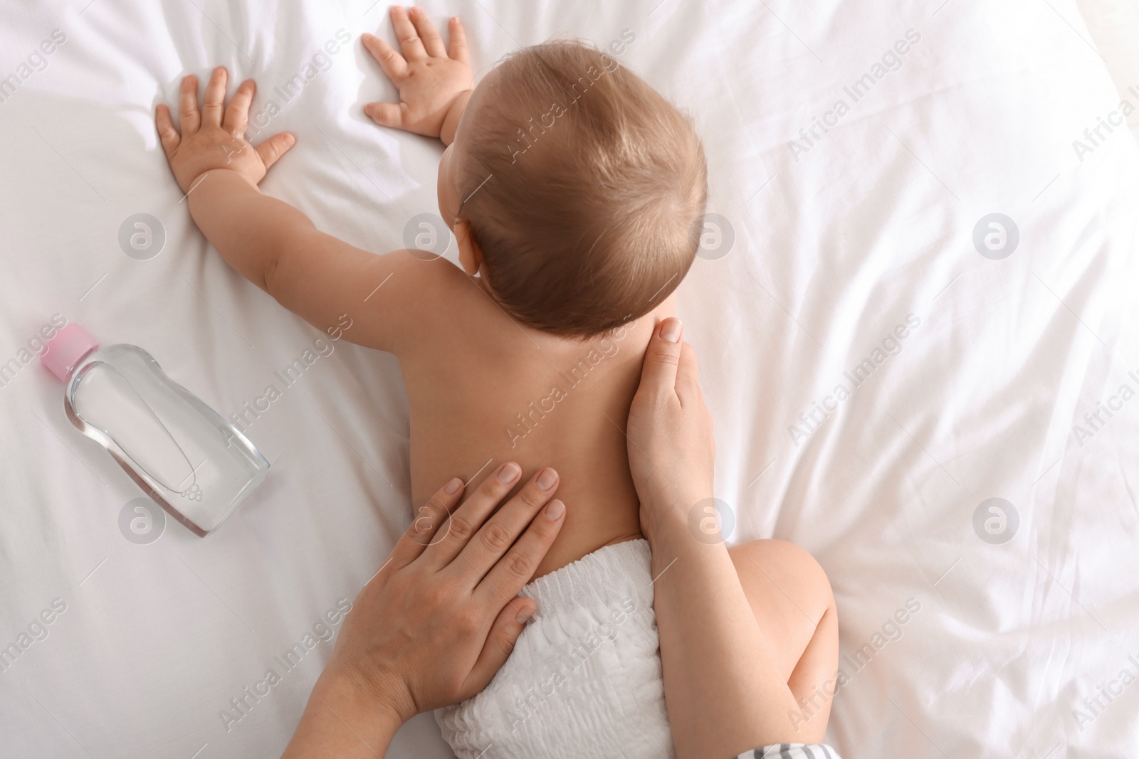 Photo of Mother massaging her cute baby with oil on bed, closeup