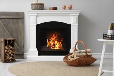 Photo of Wicker basket and crate with firewood near white fireplace in cozy living room