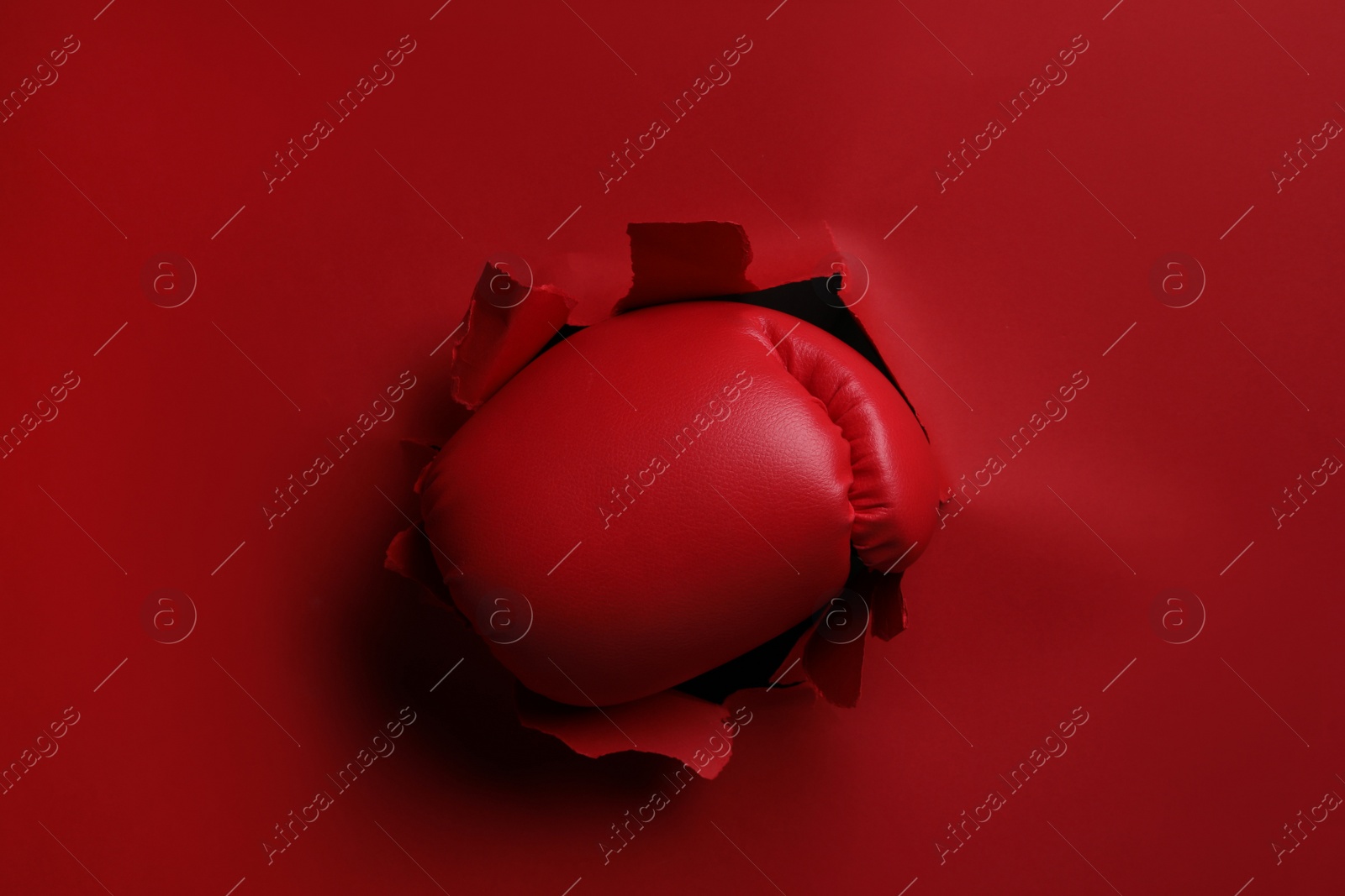 Photo of Man breaking through red paper with boxing glove, closeup