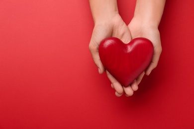 Woman holding decorative wooden heart on red background, top view