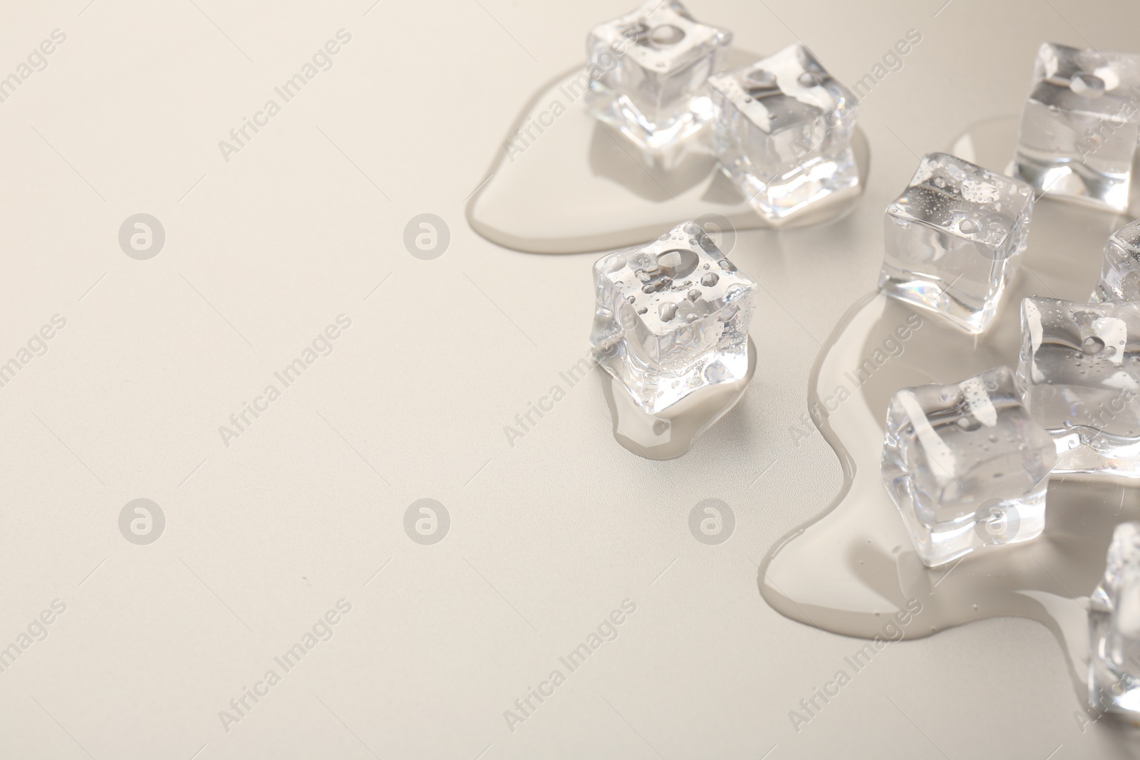 Photo of Melting ice cubes and water drops on light grey background, closeup. Space for text