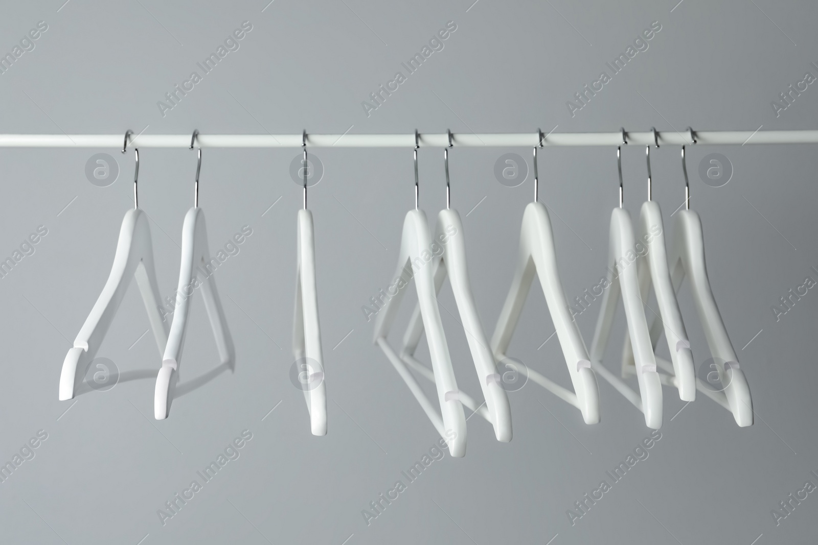 Photo of White clothes hangers on metal rail against light background