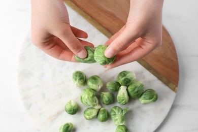 Photo of Woman separating leaf from fresh brussel sprouts at white table, top view