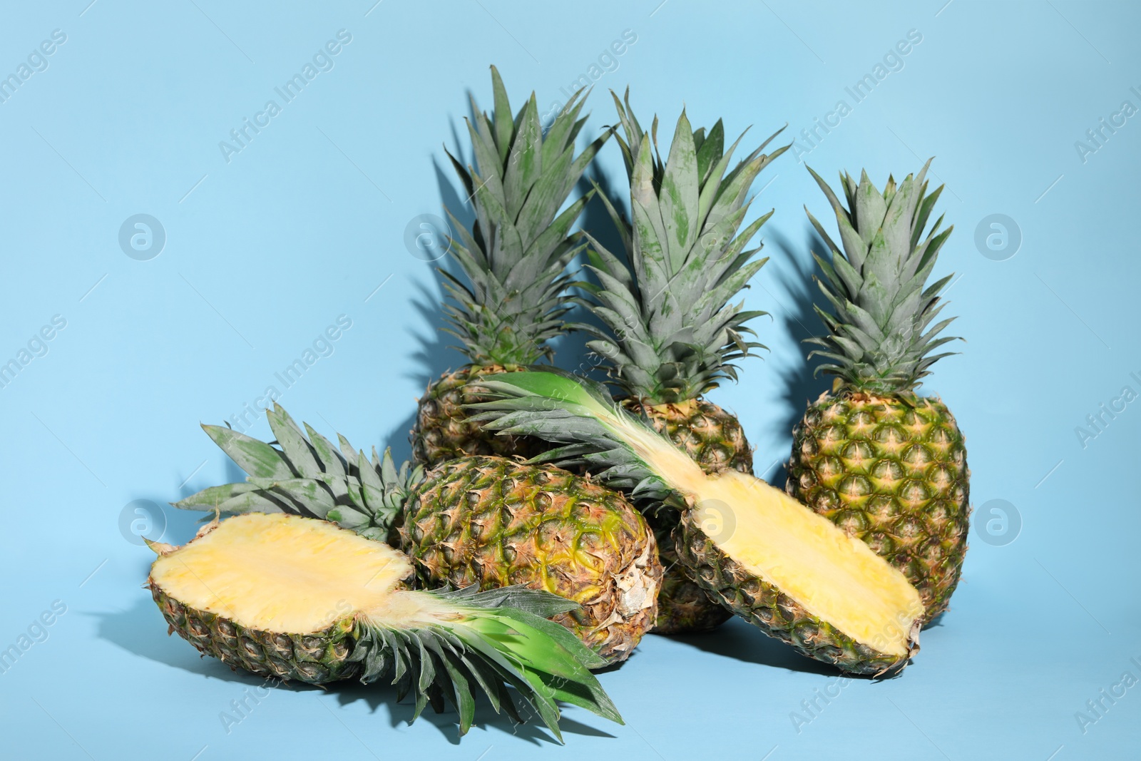 Photo of Whole and cut ripe pineapples on light blue background