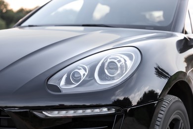 Photo of Modern black car parked outdoors, closeup view of headlight