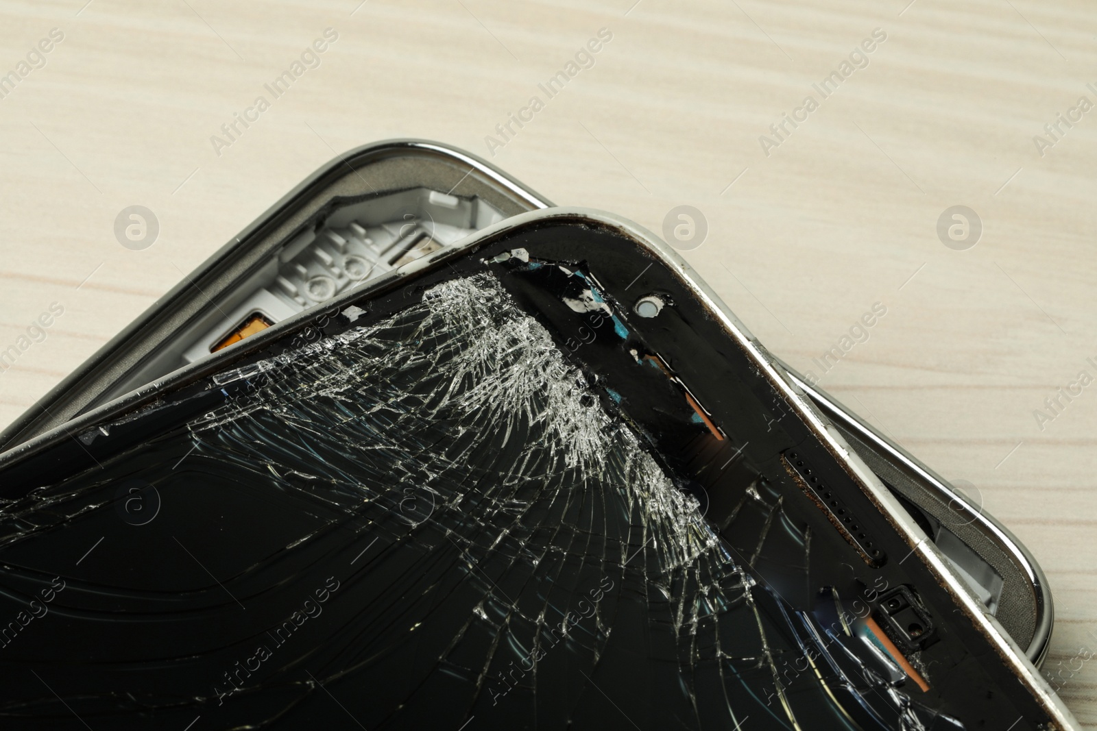 Photo of Broken smartphone on light beige wooden background, closeup. Device repair