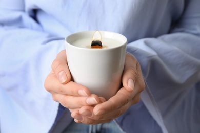 Woman holding burning candle with wooden wick, closeup