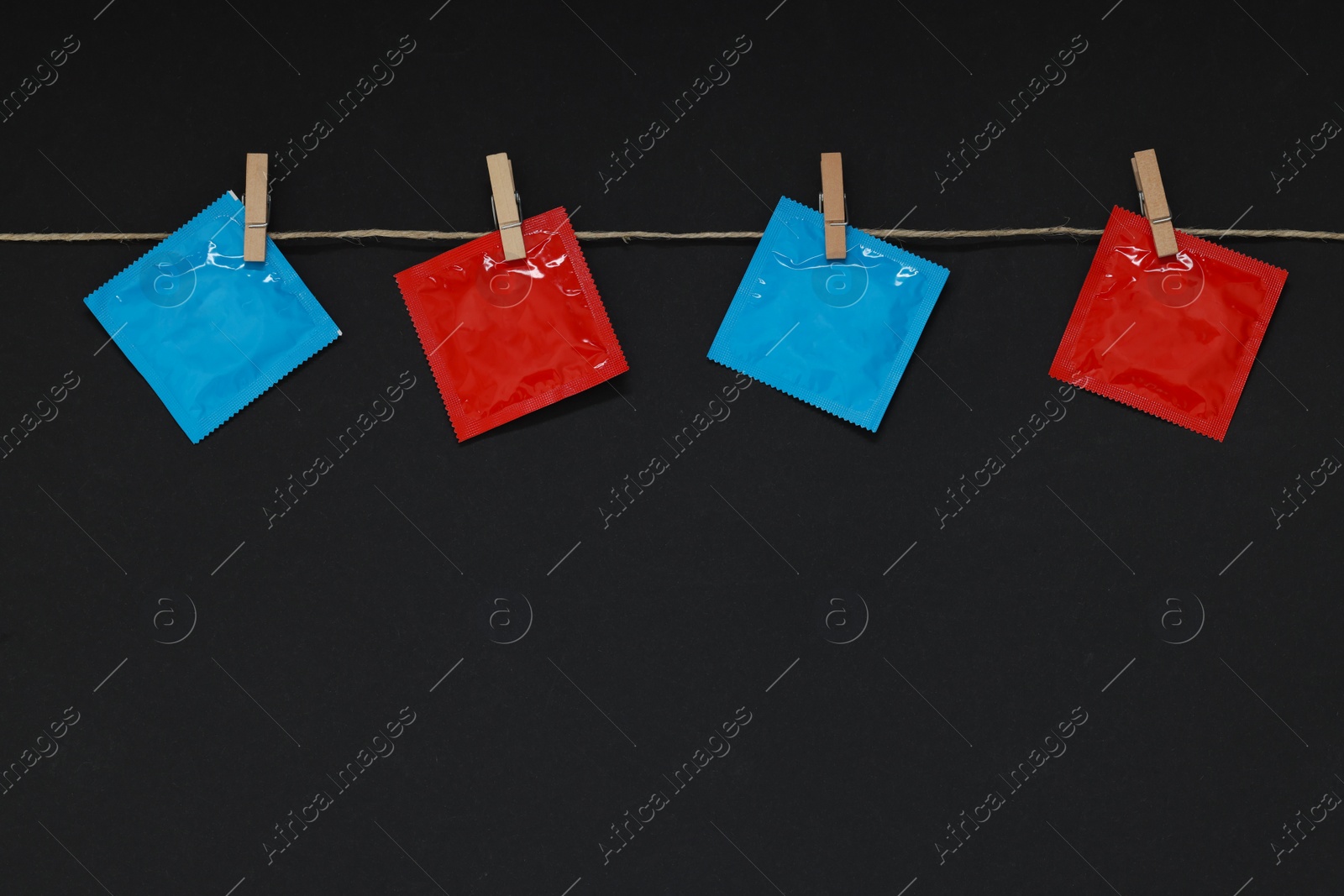 Photo of Clothesline with packaged condoms on black background, space for text. Safe sex