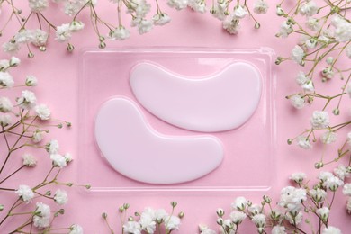 Package with under eye patches and flowers on light pink background, flat lay. Cosmetic product