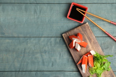 Photo of Fresh crab sticks with soy sauce served on wooden table, flat lay. Space for text