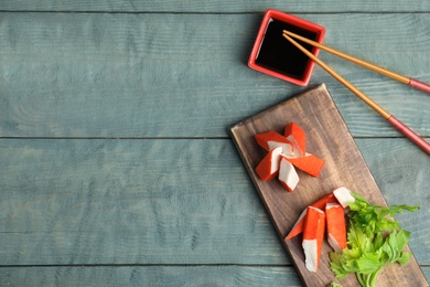 Fresh crab sticks with soy sauce served on wooden table, flat lay. Space for text