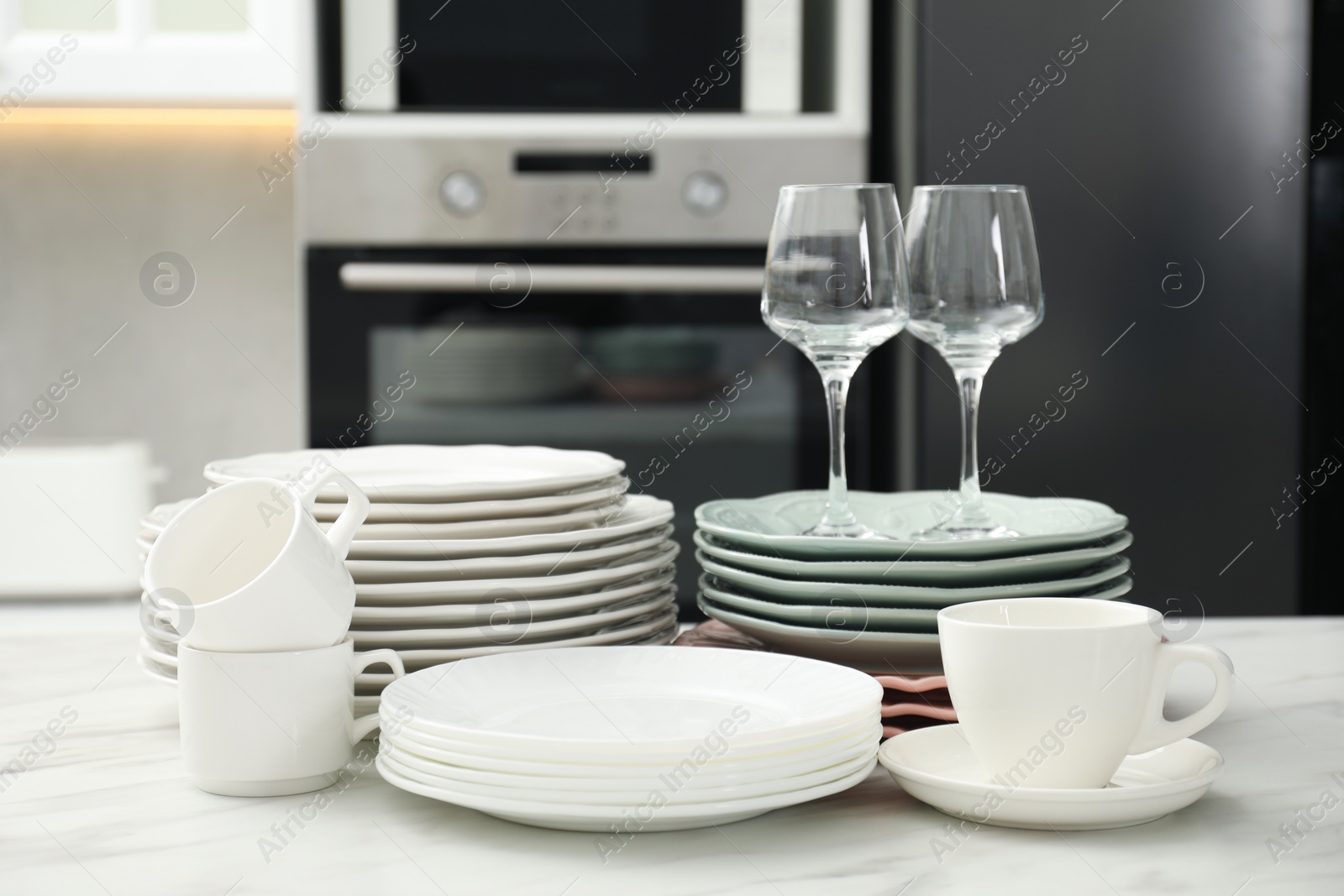 Photo of Clean plates, cups and glasses on white marble table in kitchen