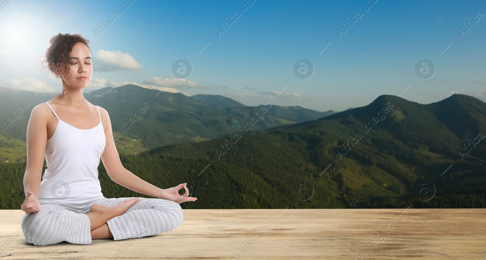 Image of Young African American woman practicing yoga on wooden surface against beautiful mountain landscape, space for text. Banner design