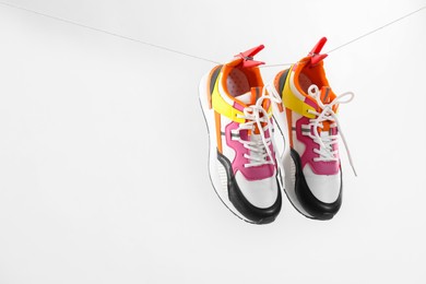 Photo of Stylish sneakers drying on washing line against light grey background, space for text