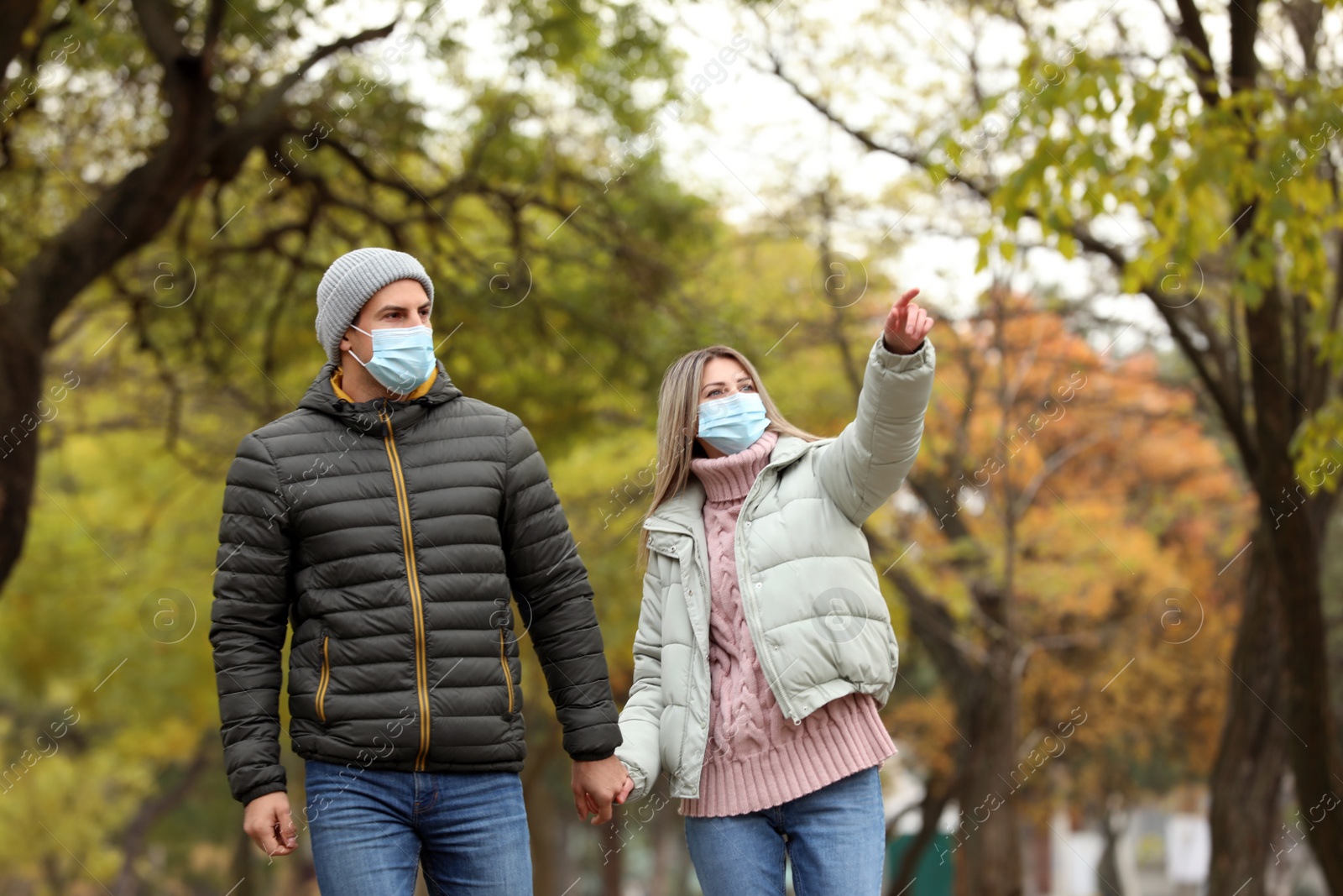 Photo of Couple in medical masks walking outdoors on autumn day. Protective measures during coronavirus quarantine