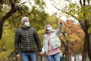 Photo of Couple in medical masks walking outdoors on autumn day. Protective measures during coronavirus quarantine