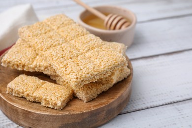 Photo of Board with tasty sesame kozinaki bars on white wooden table, closeup. Space for text