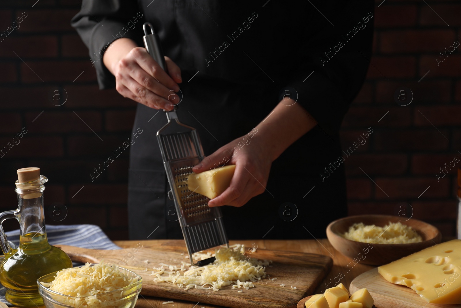 Photo of Woman grating cheese at wooden table, closeup