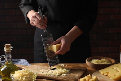 Woman grating cheese at wooden table, closeup