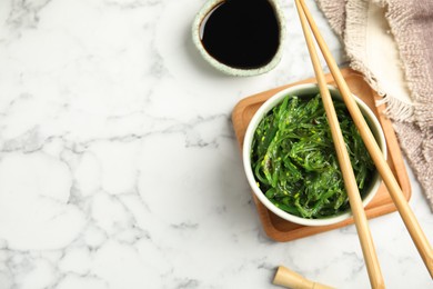 Photo of Japanese seaweed salad served on white marble table, flat lay. Space for text