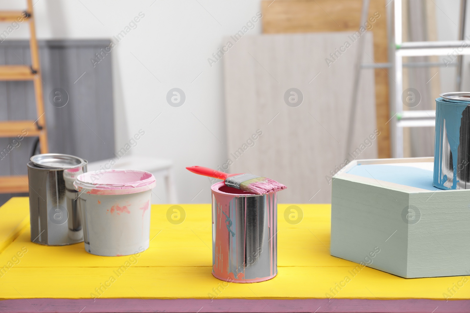 Photo of Pink paint and brush on yellow table indoors
