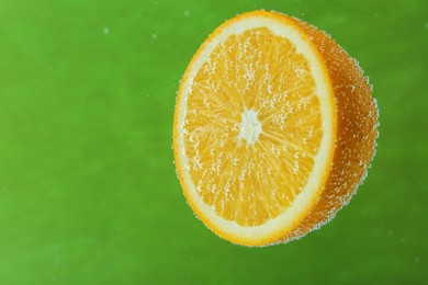 Photo of Half of orange in sparkling water on green background. Citrus soda