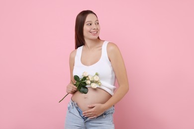 Beautiful pregnant woman with roses on pink background