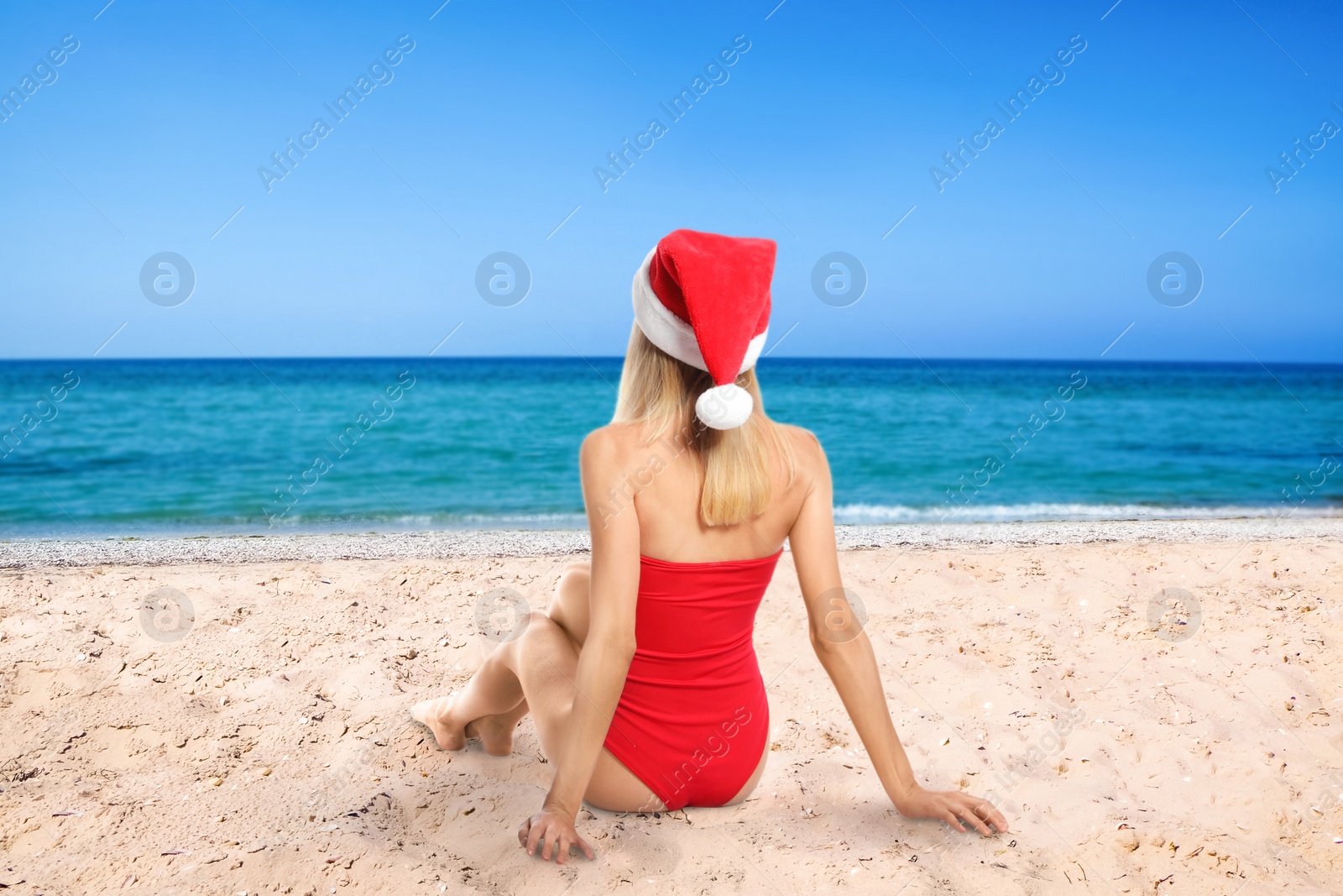 Image of Young woman wearing Santa Claus hat on beach near sea, back view. Christmas vacation