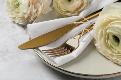 Photo of Stylish table setting with cutlery and flowers on white marble background, closeup