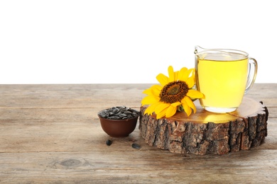 Photo of Sunflower, jug of oil and seeds on wooden table against white background, space for text