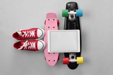 Modern tablet, skateboards and shoes on light grey background, flat lay. Space for text