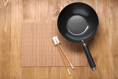 Empty iron wok and chopsticks on wooden table, top view. Space for text