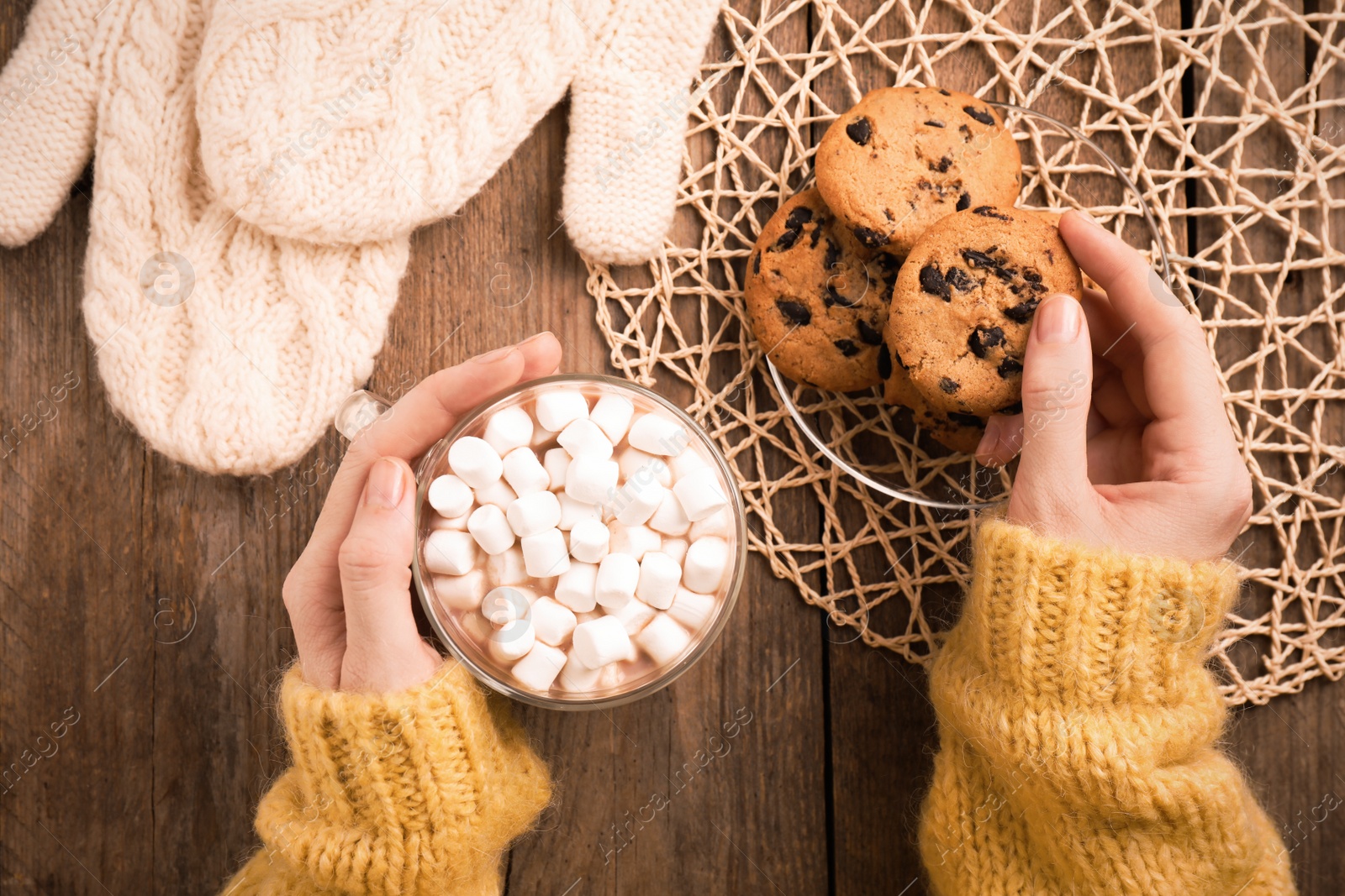 Photo of Woman with cup of delicious marshmallow cocoa and cookies at wooden table, top view