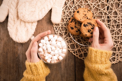 Photo of Woman with cup of delicious marshmallow cocoa and cookies at wooden table, top view